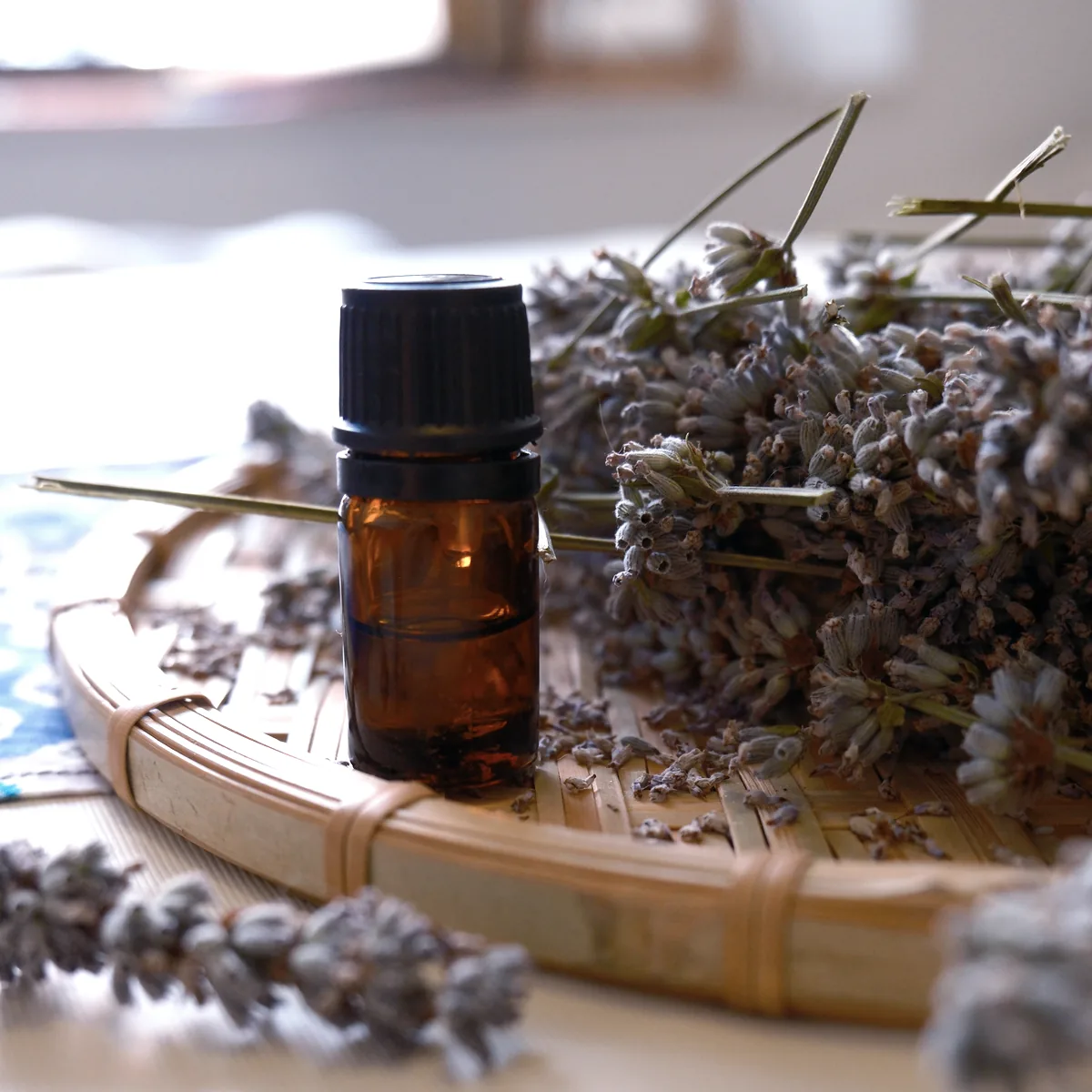 An amber bottle of essential oil resting on pale wood beside dried lavender