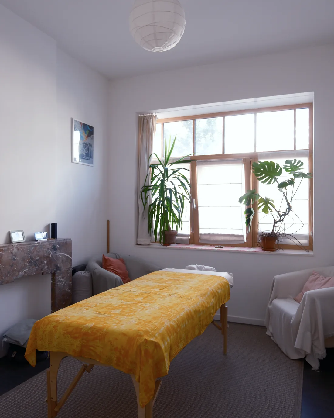 The practice room: the massage table dressed in a yellow sarong under a bright window, plants on the sill